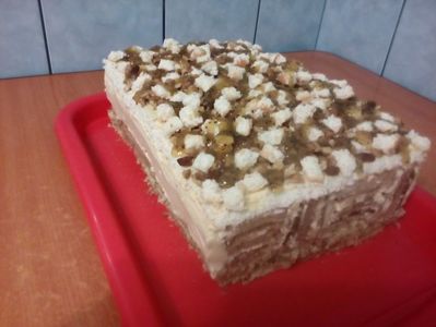 Prăjitură cu foi răsturnate; Blat cu mac, blat de bezea cu cocos, foi de cacao, crema de vanilie, cremă cu ciocolată, decor: nuci, stafide, bucățele de blat de bezea și dulceață de kivi.
